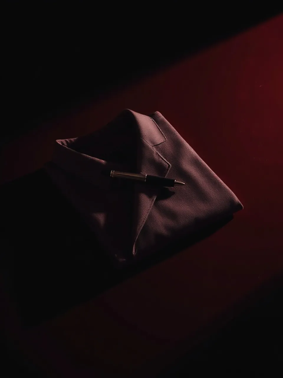 Folded blazer with brushed-steel pen laid across, on polished claret lacquer